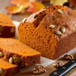 Classic Libby's Pumpkin Bread Recipe: A freshly baked loaf of moist pumpkin bread, golden brown with a slightly cracked top, surrounded by warm fall colors like cinnamon sticks and orange pumpkins, capturing the essence of autumn's cozy flavors.