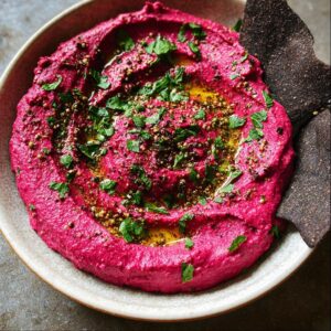 Bowl of Bloody Beet Hummus topped with herbs and served with bat-shaped pita chips.
