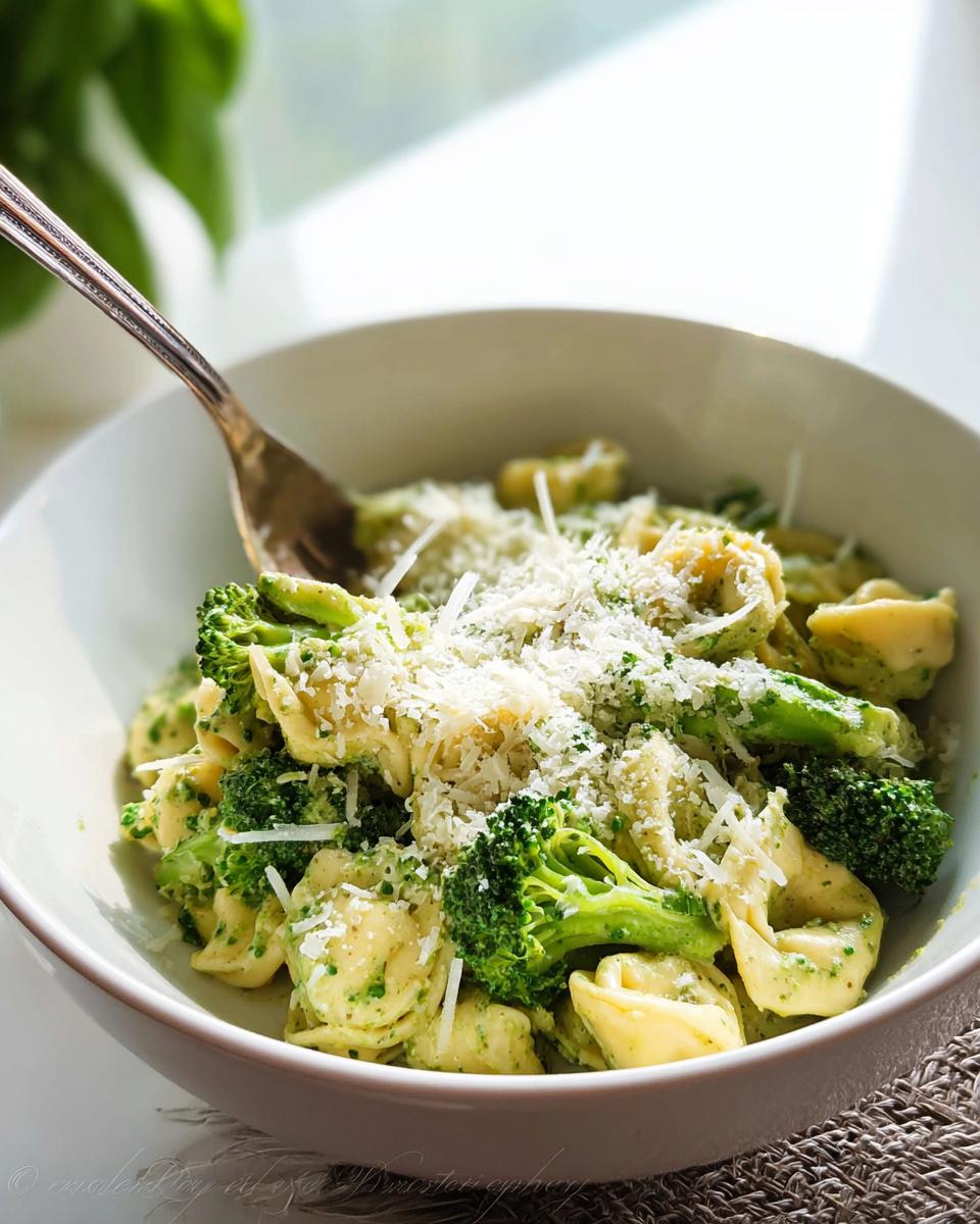 Bowl of creamy pesto tortellini topped with broccoli and cheese.