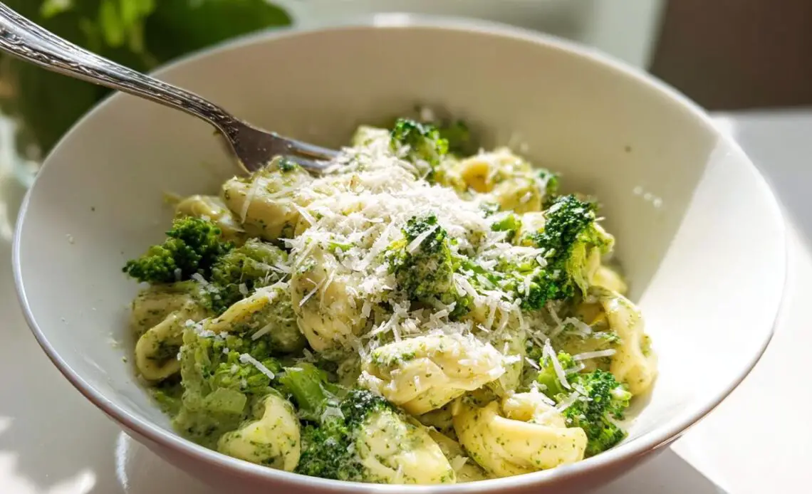 Bowl of creamy pesto tortellini with spinach and broccoli topped with cheese.