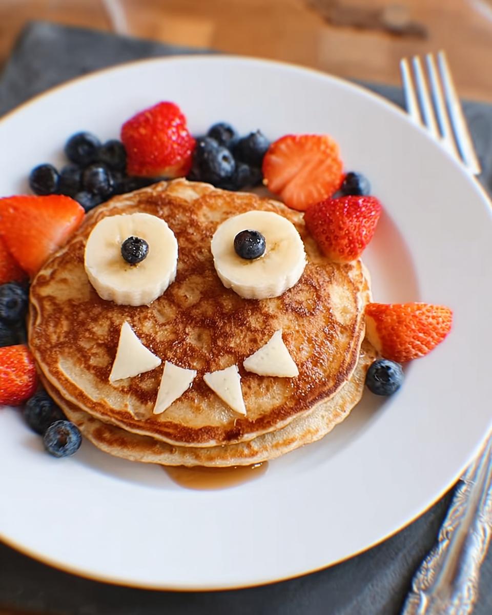 Colorful monster pancakes decorated with banana eyes and berries.