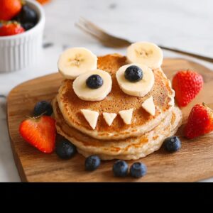 Stack of monster pancakes decorated with banana eyes and berry features.